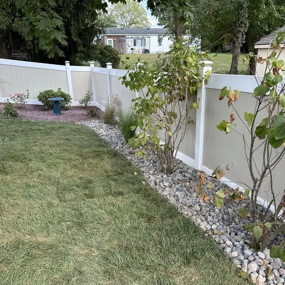 Newly sodded side lawn along a white vinyl fence with a stone-edged planting bed