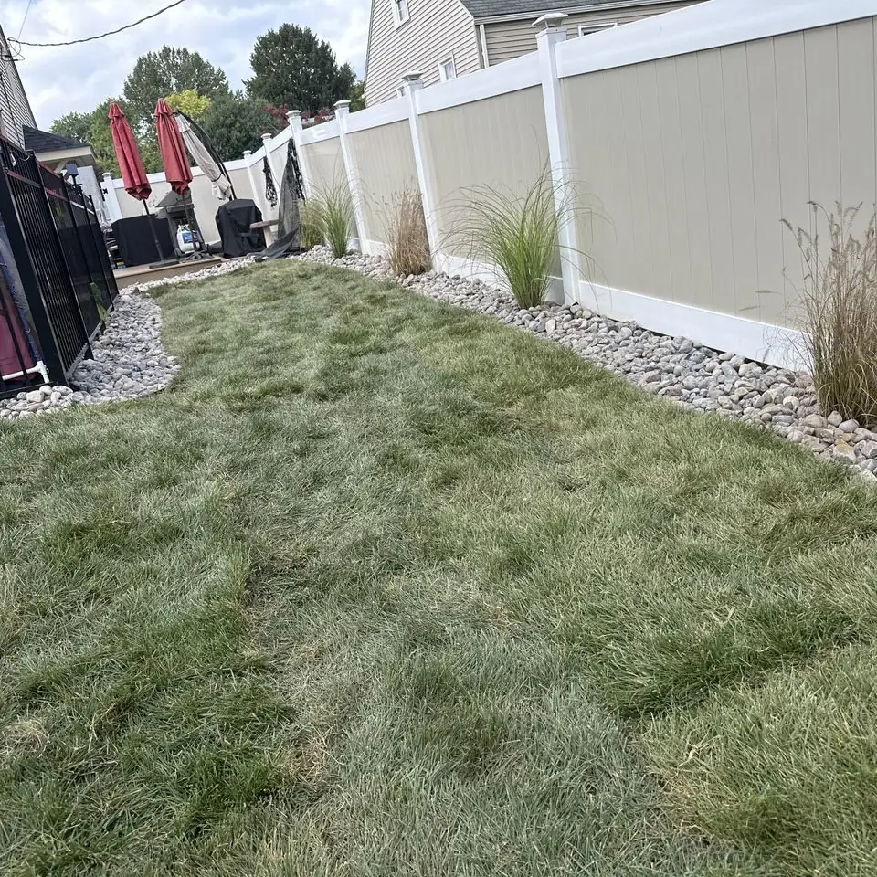 Graded lawn with stone edging and ornamental grasses along a vinyl fence